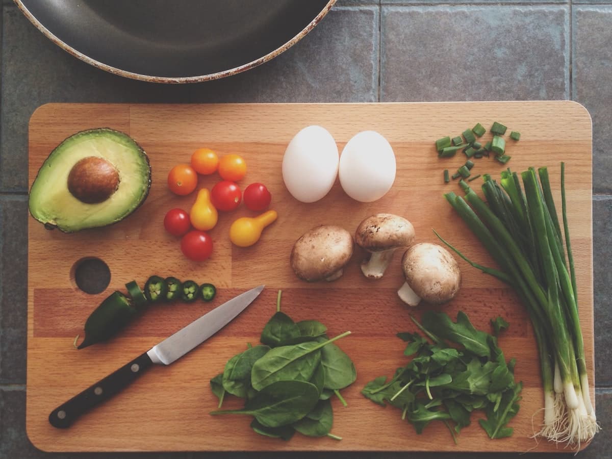 Planche à découper avec avocat, tomates cerises, œufs, champignons et herbes fraîches