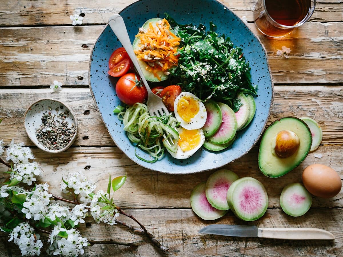 Assiette équilibrée avec œuf, légumes verts, tomates et radis sur une table en bois